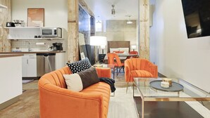 A modern living room with an orange sofa, a glass coffee table, and a dining area with orange chairs.
