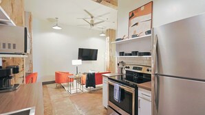 A compact kitchen with a refrigerator, oven, microwave, and a TV mounted on the wall.