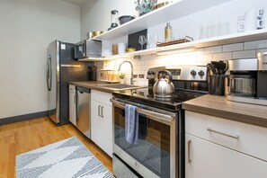 A modern kitchen with stainless steel appliances, white cabinetry, and a wooden countertop. - Exquisite White Lily in Old City (Knoxville)
