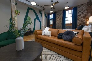 A modern lounge with a leather sofa, green armchair, and a round table with a vase. - Exquisite White Lily in Old City (Knoxville)