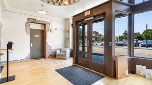 A modern interior with a wooden floor, a grey sofa, a black door with an 'EXIT' sign, and a view of the street outside.