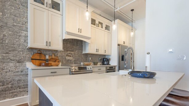 A modern kitchen with white cabinets, a large island, and a brick accent wall. - Historic Elegance on Gay Street (Knoxville)