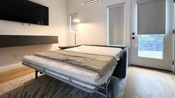 A bedroom with a bed, a TV mounted on the wall, an air conditioner, and a door leading to a balcony.
