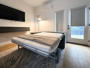 A bedroom with a bed, a TV mounted on the wall, an air conditioner, and a door leading to a balcony.