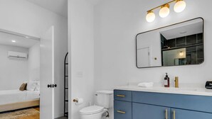 Une salle de bain moderne avec des toilettes blanches, un meuble-lavabo bleu doté de poignées dorées et un miroir au-dessus du lavabo.