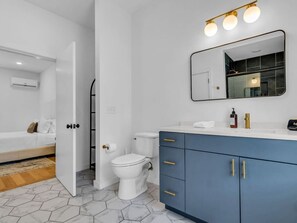 A modern bathroom with a white toilet, a blue vanity with gold handles, and a mirror above the sink.