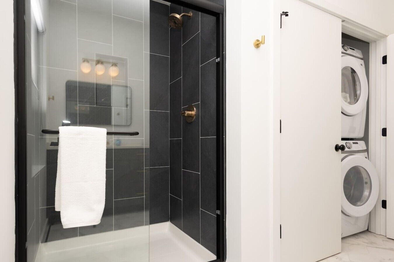 Une salle de bain moderne avec une douche à parois de verre, une serviette blanche et un lave-linge visible dans la pièce adjacente.