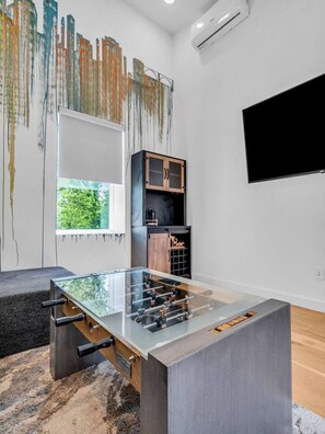 A modern room with a foosball table, a television, and a window with a view of greenery. - Luxury Townhouse w/Rooftop (Knoxville)