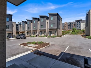 A modern apartment complex with a central courtyard, a paved driveway, and a vehicle parked in the lot.