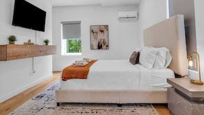 Une chambre à coucher moderne avec un lit, une table de chevet et un téléviseur fixé au mur.