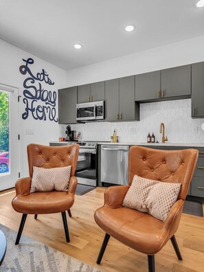 A modern kitchen with grey cabinets, a microwave, and a sink. There are two leather chairs with cushions. - Luxury Townhouse w/Rooftop (Knoxville)