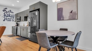 Une cuisine moderne avec des meubles gris, un réfrigérateur noir et un coin repas comprenant une table ronde et des chaises grises.