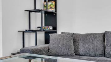 Une table de baby-foot dans un salon moderne, avec un canapé gris et une étagère noire en arrière-plan.