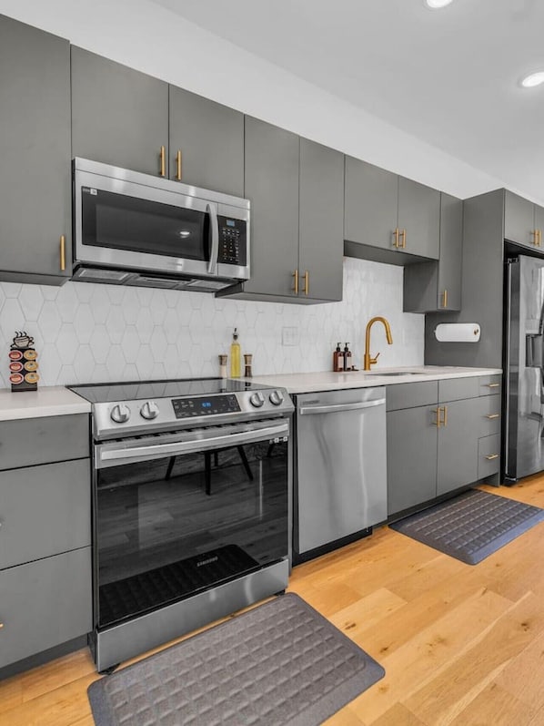 A modern kitchen with grey cabinets, stainless steel appliances, and a wooden floor.