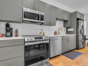 A modern kitchen with grey cabinets, stainless steel appliances, and a white countertop. - Luxury Townhouse w/Rooftop (Knoxville)