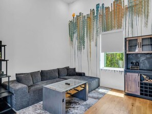 A modern living room with a grey sectional sofa, a glass coffee table, and a wooden cabinet. - Luxury Townhouse w/Rooftop (Knoxville)