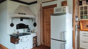 A kitchen with a stove, oven, and refrigerator. There is a wooden door and a shelf with kitchen utensils. - 3 bedroom lovely home in Likenäs (Likenäs)