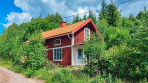 A red wooden house with a sloped roof, surrounded by dense greenery and trees. - 3 bedroom lovely home in Likenäs (Likenäs)