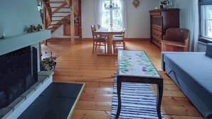 A cozy living room with a fireplace, wooden flooring, a dining table with chairs, a sofa, and a patterned rug. - 3 bedroom lovely home in Likenäs (Likenäs)