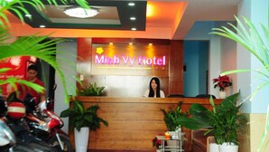 Una recepción en el Hotel Minh Vy con un letrero de neón, plantas en macetas y una lámpara en el techo.