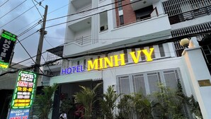 Un hotel llamado "Minh Vy" con una fachada moderna, varios balcones y plantas en macetas en la entrada.