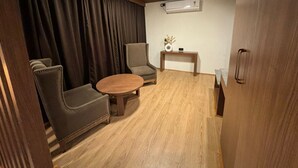 A room with a wooden ceiling, a round wooden table, two armchairs, a small side table with a vase, and an air conditioning unit on the wall. - The Magnolia Srinagar (Srinagar)
