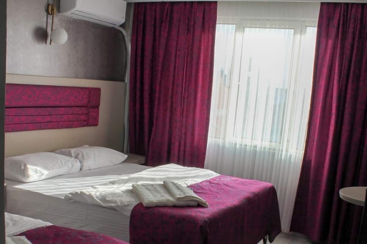 Habitación de hotel con dos camas, cabecera, ventana con cortinas y una mesita.