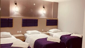 A hotel room with four beds, each with a purple bedspread and white linens. There are wall-mounted light fixtures above each bed. - Seta Park Hotel (Inegöl)