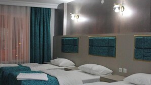 A hotel room with four single beds, each with a teal bedspread and white pillows. There are two wall-mounted light fixtures above the beds. - Seta Park Hotel (Inegöl)