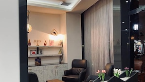A modern living room with a marble floor, leather sofas, a coffee table, and a fireplace. There is a bookshelf with decorative items and a large window with curtains. - Seta Park Hotel (Inegöl)