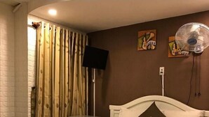 A neatly made bed with a brown bedspread and a pillow with a logo, a wall-mounted fan, and a painting on the wall. - An Chi Hotel SG - by BAY LUXURY (Ho Chi Minh City)