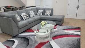 Een woonkamer met een grijze modulaire bank, een glazen salontafel en een kamerbreed tapijt met een patroon.