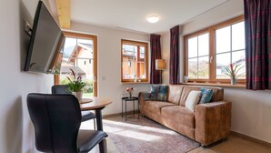 A living room with a sofa, a chair, a small table, and a TV mounted on the wall.
