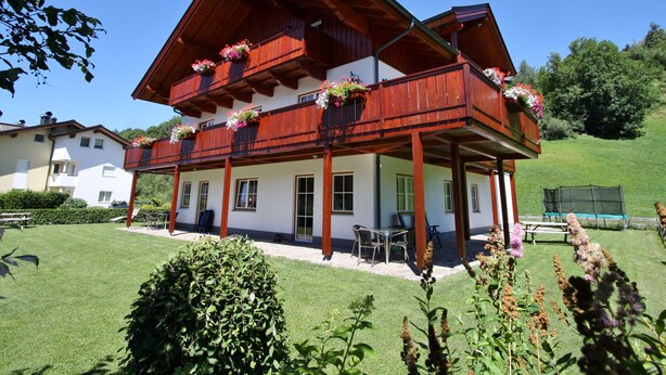 A two-story chalet with wooden balconies, a covered patio, and a well-maintained lawn.