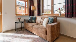 A cozy living room with a brown sofa, a small side table with a lamp, and a window with curtains.
