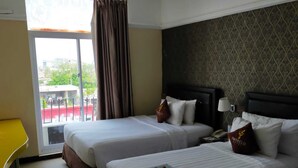 Una habitación de hotel con dos camas, un escritorio amarillo, una ventana con cortinas y un papel tapiz estampado.