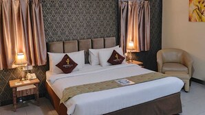 Habitación de hotel con una cama grande, dos lámparas de noche, una silla y papel tapiz estampado.