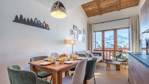 A dining area with a wooden table, chairs, and a view of mountains through large windows. - Pégase 407 - Le Cima - Duplexe luxe Belle Plagne (La Plagne-Tarentaise)