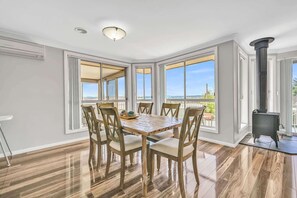 Un comedor con una mesa grande y sillas, ventanas amplias con vistas y un estufa de leña.