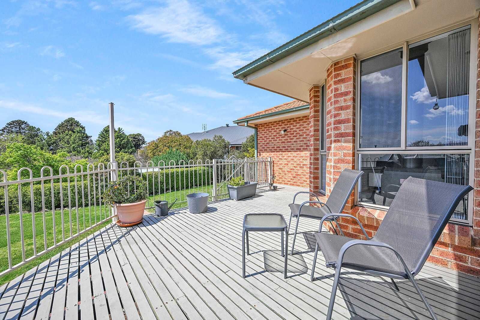 A wooden deck with outdoor seating, a brick building, and a metal fence.