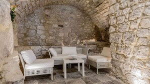 A stone-walled room with a white wicker sofa set, a small table, and a stone floor.
