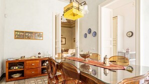 A dining area with a glass table, wooden chairs, a wooden cabinet, and a yellow pendant light.