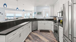 A modern kitchen with white cabinets, stainless steel appliances, and a black countertop. - Cala Tortuga Beachfront Elevator, Hot Tub, Great Views (Galveston)