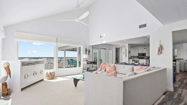 A spacious living room with a large window, a ceiling fan, and a view of the sky. - Cala Tortuga Beachfront Elevator, Hot Tub, Great Views (Galveston)