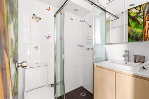 Ein modernes Badezimmer mit Duschkabine aus Glas, weißen Fliesen und einem Waschtisch mit beige lackiertem Unterschrank.