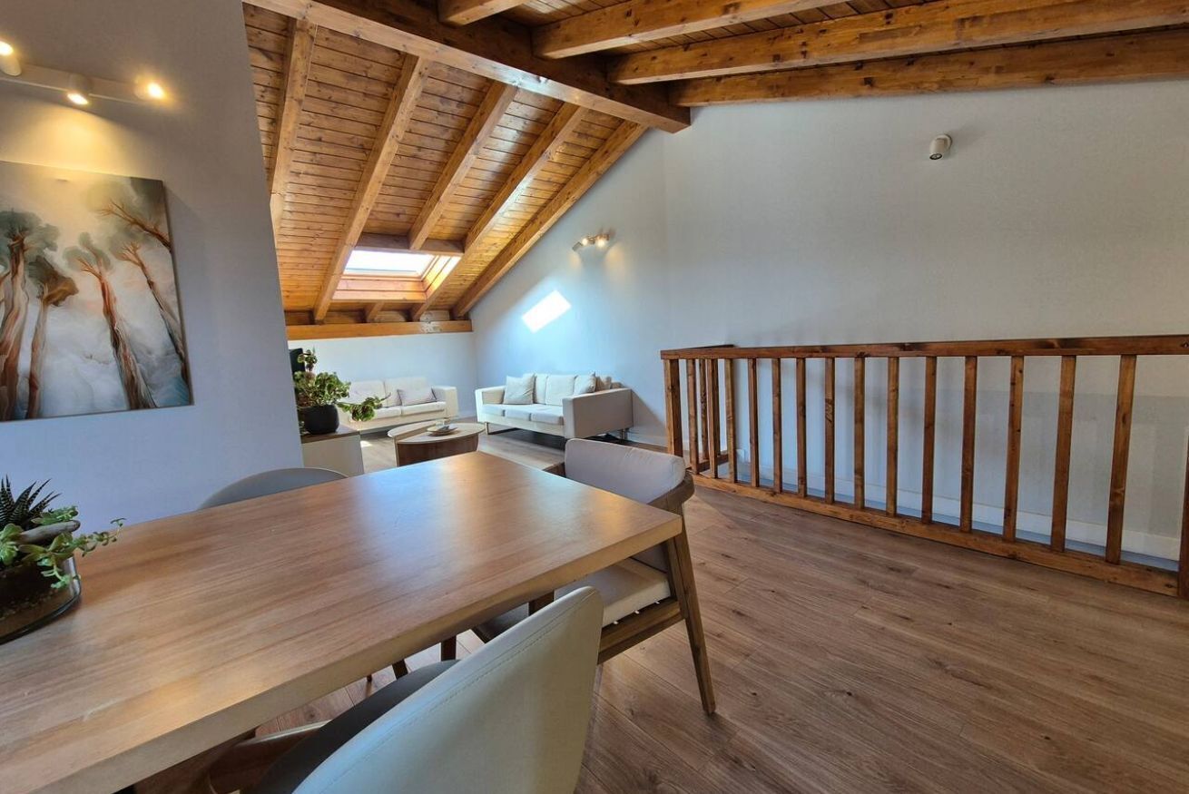 Een eetgedeelte met een houten tafel en stoelen, een witte bank en een houten leuning.