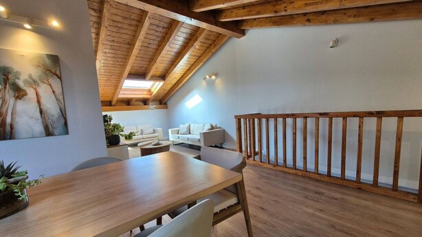 Een eetgedeelte met een houten tafel en stoelen, een witte bank en een houten leuning.