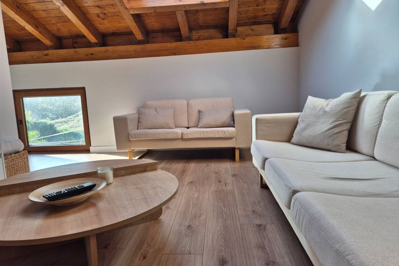Un soggiorno moderno con soffitto in legno, due divani beige, un tavolino rotondo e un telecomando sopra.