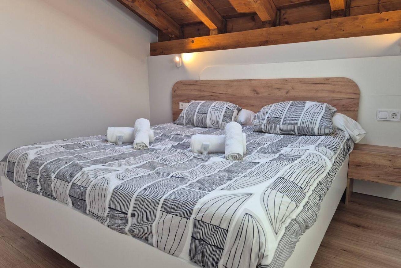 Un letto rifatto con cura, con copripiumino a righe e cuscini, una testiera in legno e un comodino con una lampada.