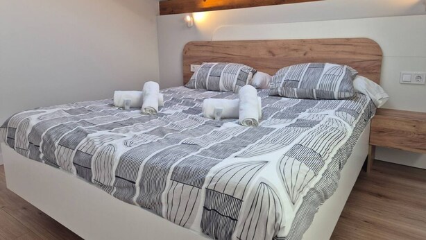 A neatly made bed with a striped bedspread and pillows, a wooden headboard, and a bedside table with a lamp. - C26A01 Apto Moderno en Tagle (Tagle)